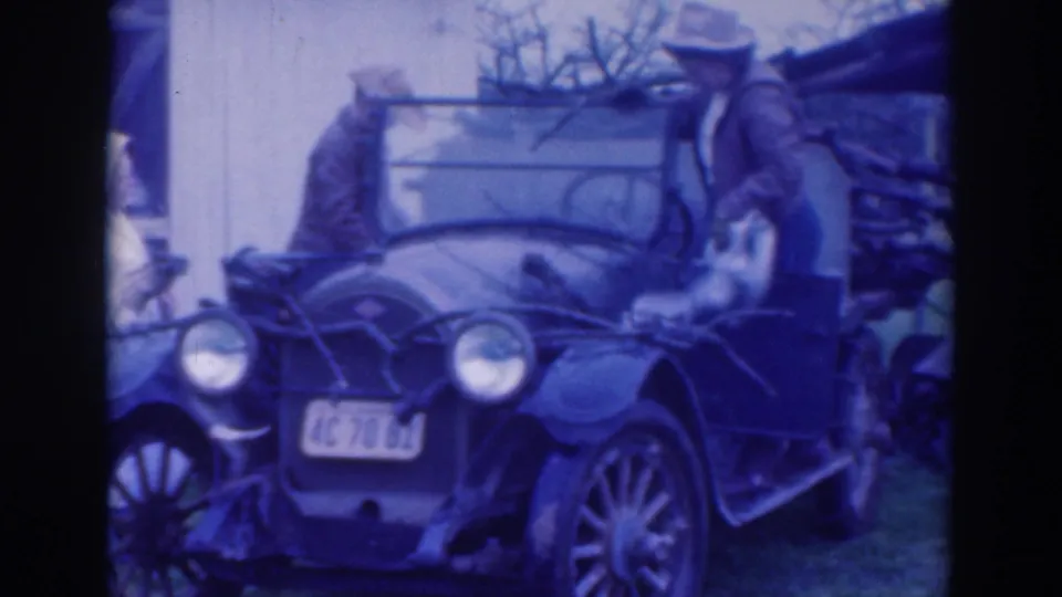 In 1937 Sacramento home-movie footage, two adult men stand beside an open vintage car with round headlights and a visible California plate.