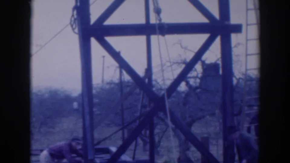 A worker bends at the base of the wooden construction frame while another figure is partly visible at the edge of the 1937 Sacramento scene.
