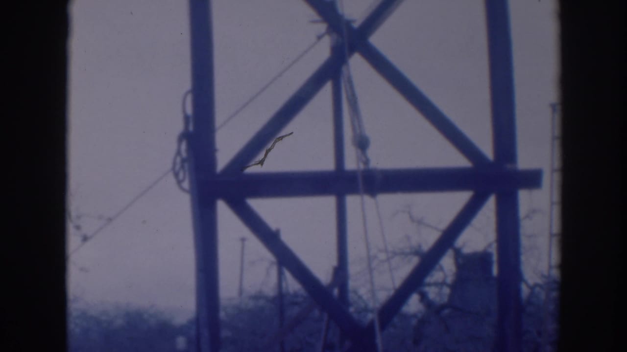 Tower cross-bracing, ropes, and ladder partly framed by dark film edges.