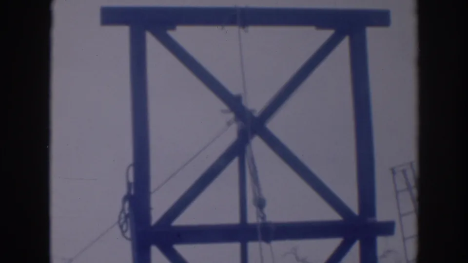 1937 Sacramento home-movie frame showing a wooden tower structure with crossed bracing, ropes, and pulley lines in soft blue-tinted focus.