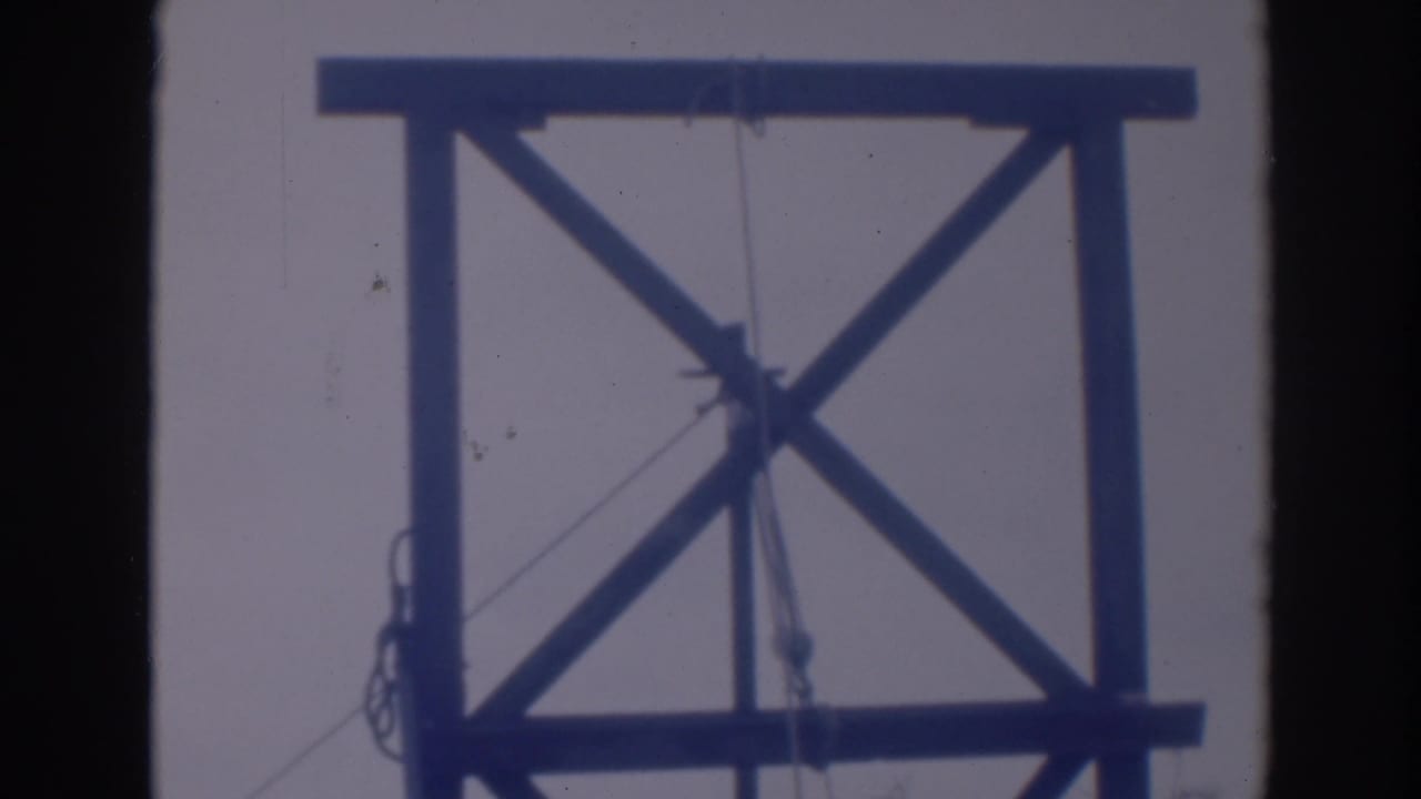 Wooden tower frame with diagonal braces, ropes, and a ladder partly visible at the side.