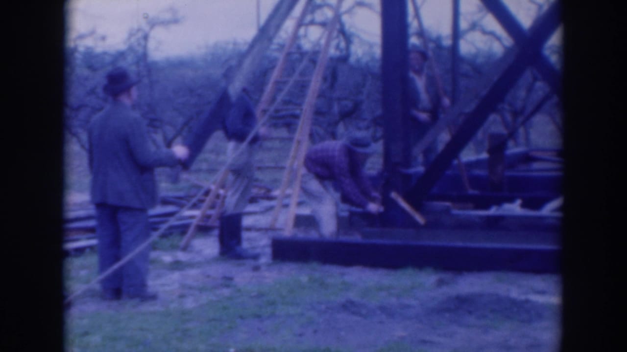 Men work near ladders and timber framing in an open field.