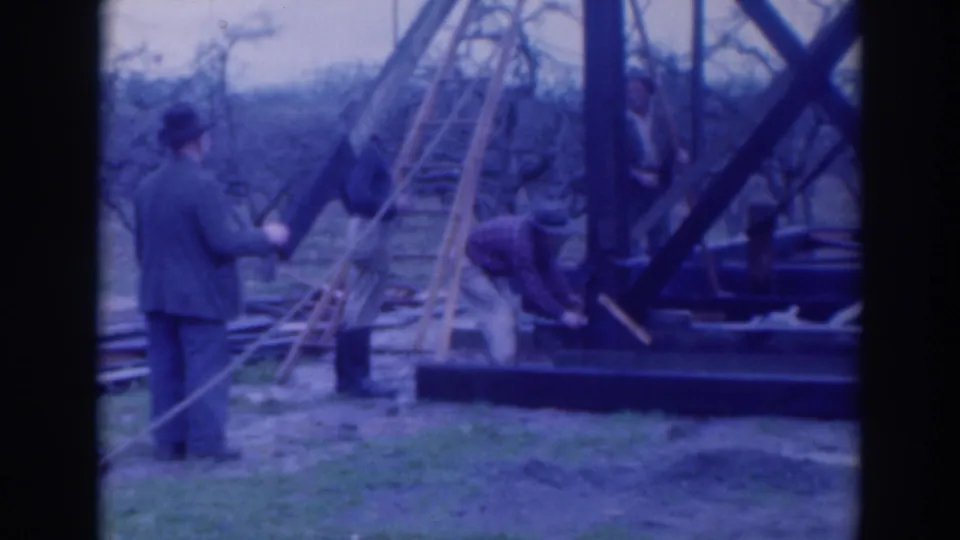 In 1937 Sacramento home-movie footage, men in hats work around ladders, ropes, and dark timber framing in an open field.