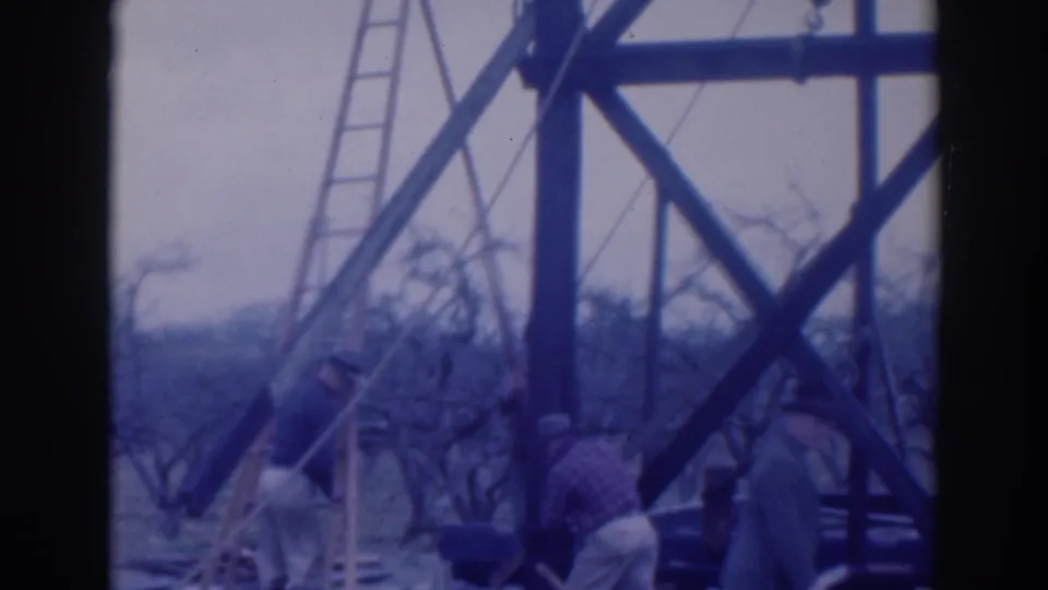 In 1937 Sacramento home-movie footage, men in hats stand near a ladder and timber frame among orchard trees.