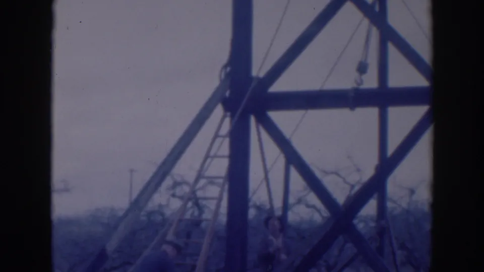 A worker in a brimmed hat appears below a ladder and heavy timber bracing in the Sacramento orchard scene.