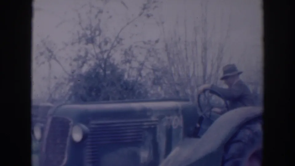 In the supplied 1937 Sacramento footage, a man drives or sits on an older tractor beside brush and orchard growth.