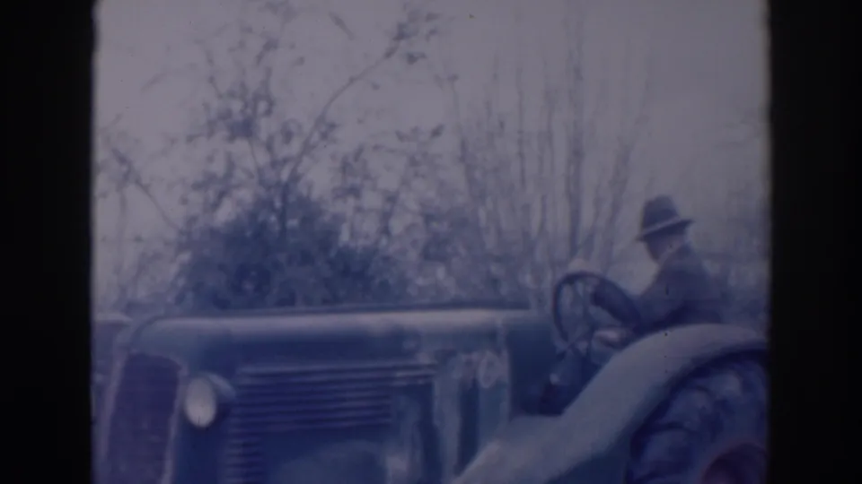 1937 Sacramento home-movie frame showing an older man in a fedora seated at the controls of a tractor in a rural setting.