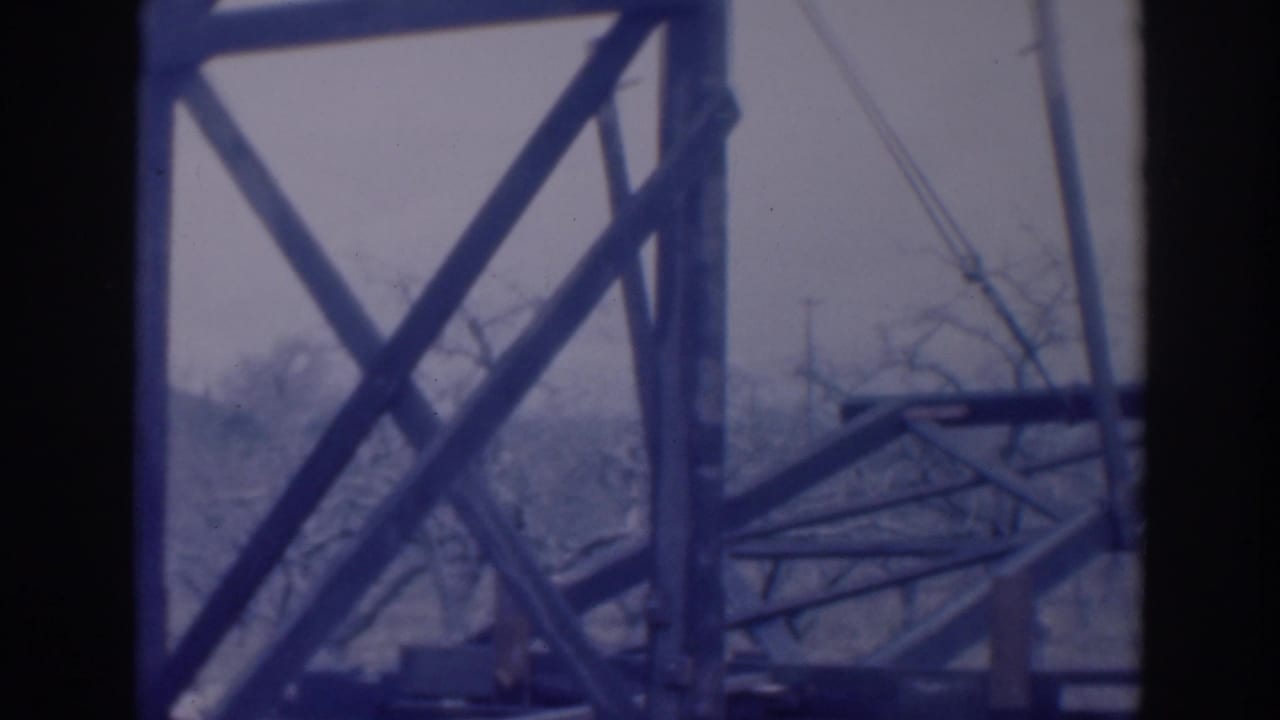 Close view of crossed steel beams and cables with bare trees behind them.