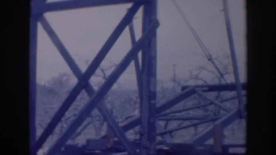 1937 Sacramento 8mm frame showing a close, soft-focus view of crossed steel members, cables, bare trees, and hazy sky.