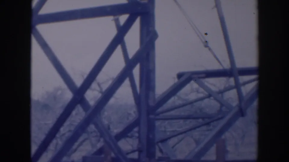 Aged 8mm frame from Sacramento in 1937 showing steel supports, cable lines, bare trees, and dark borders from the filmed viewpoint.