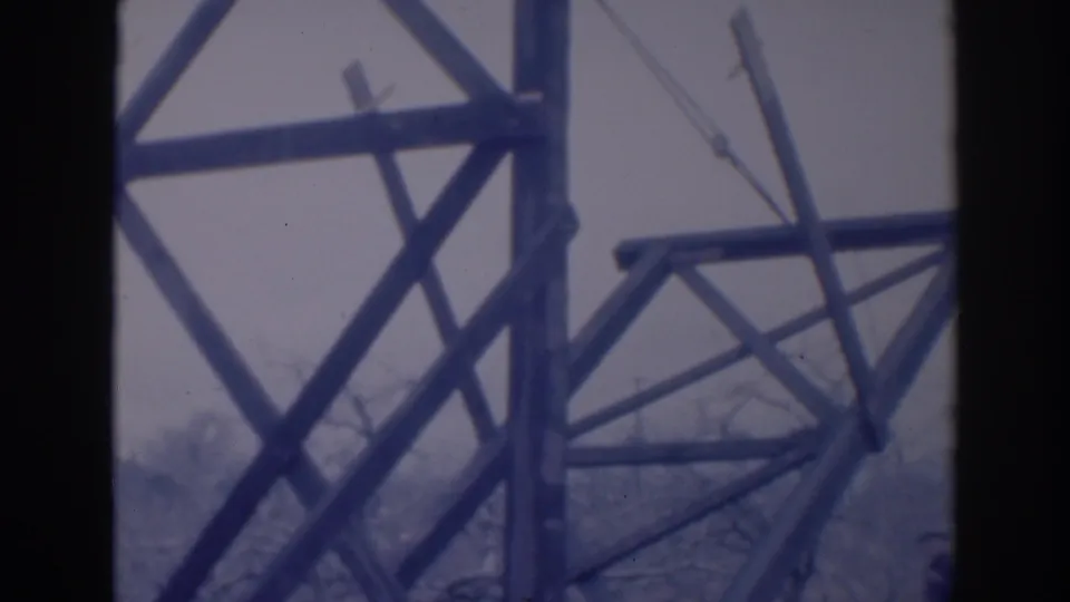 1937 Sacramento home-movie frame with angled wooden supports and a tall upright structure viewed from behind a dark interior or window edge.