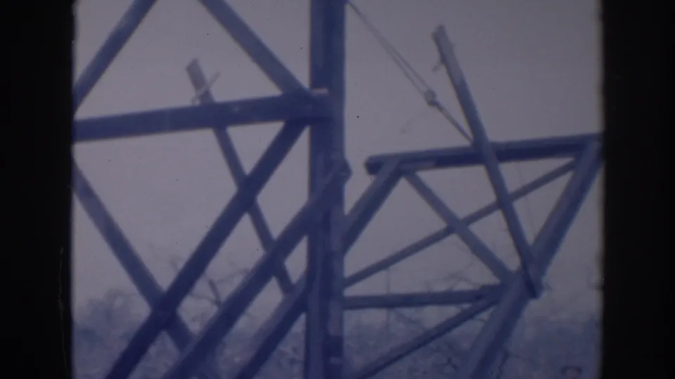 1937 Sacramento 8mm still of a wooden construction frame, with diagonal bracing, a vertical member, and bare trees beyond the work area.