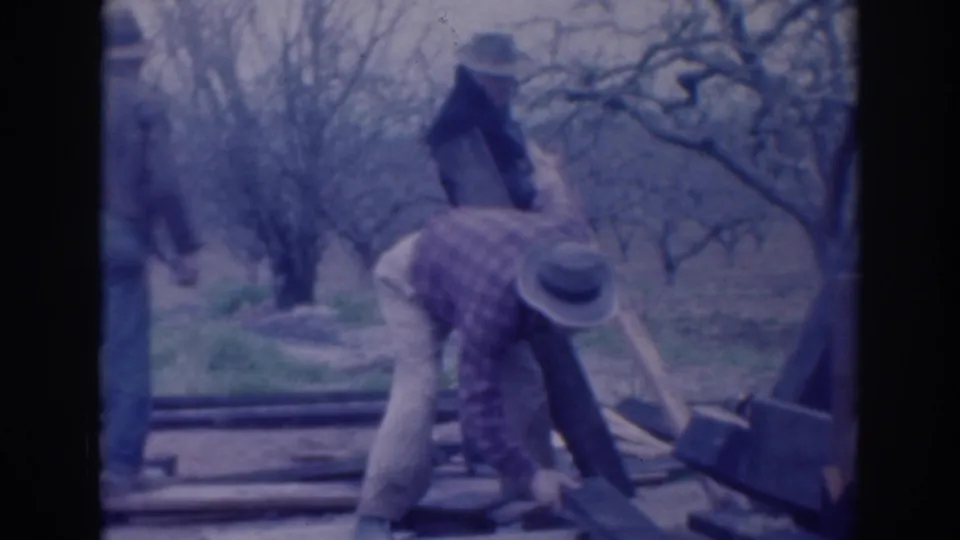 The final frame shows men continuing to handle lumber and a beam in the Sacramento orchard setting, filmed in soft faded 8mm color.
