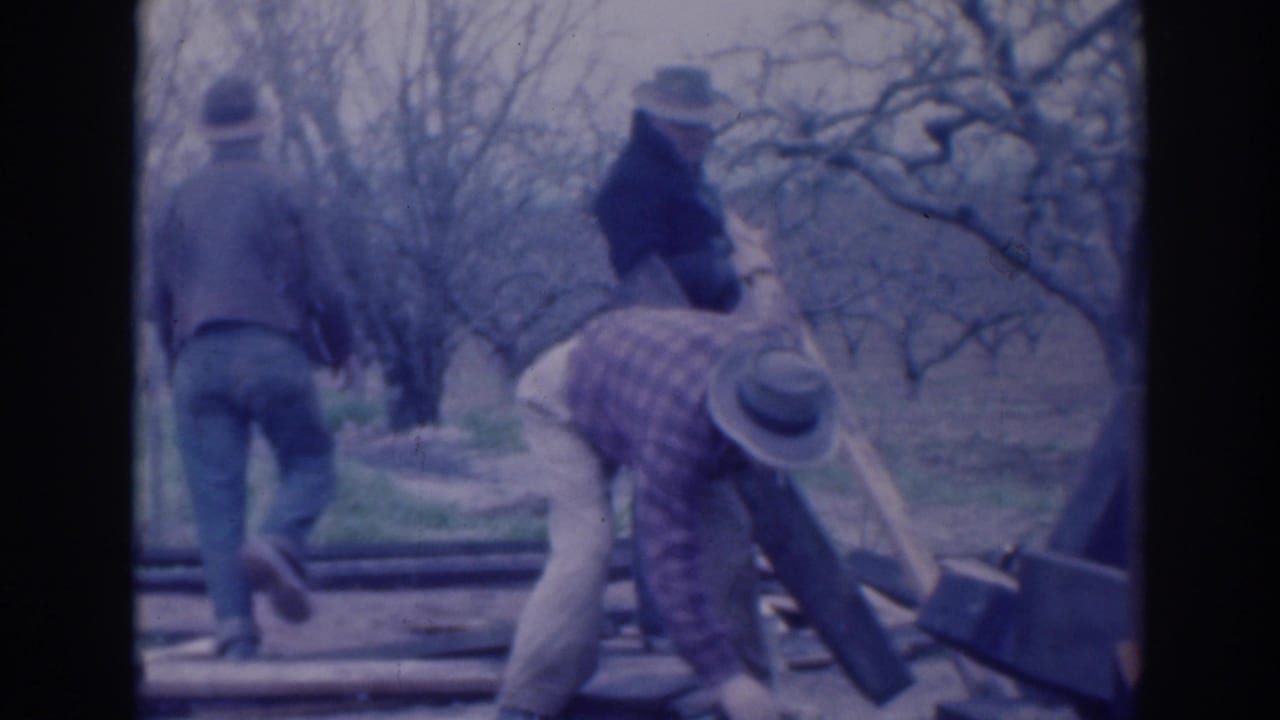 In 1937 Sacramento home-movie footage, three adult men in hats and work clothes handle wooden boards in a leafless rural setting.