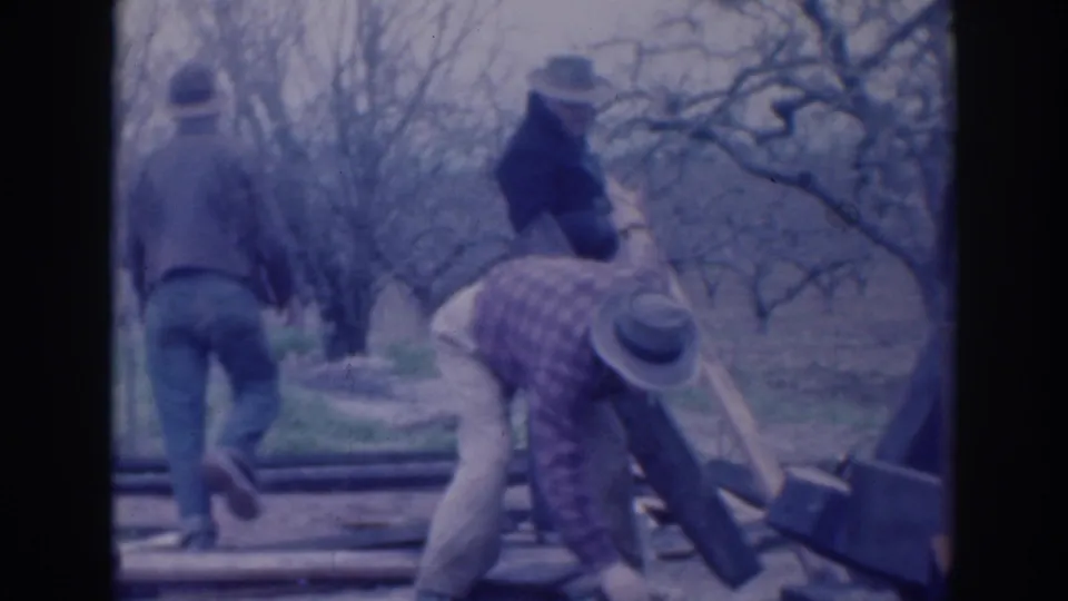 In 1937 Sacramento home-movie footage, three adult men in hats and work clothes handle wooden boards in a leafless rural setting.
