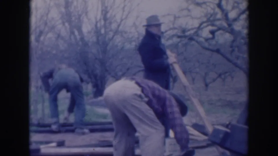 Three men in period work clothes adjust boards on the ground while one stands with a long-handled tool in Sacramento footage from 1937.