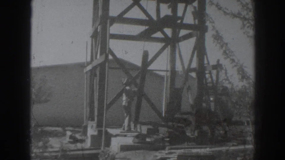 1937 Sacramento frame showing a construction worker beside a wooden derrick, with bracing, cables, and a ladder-like element visible.