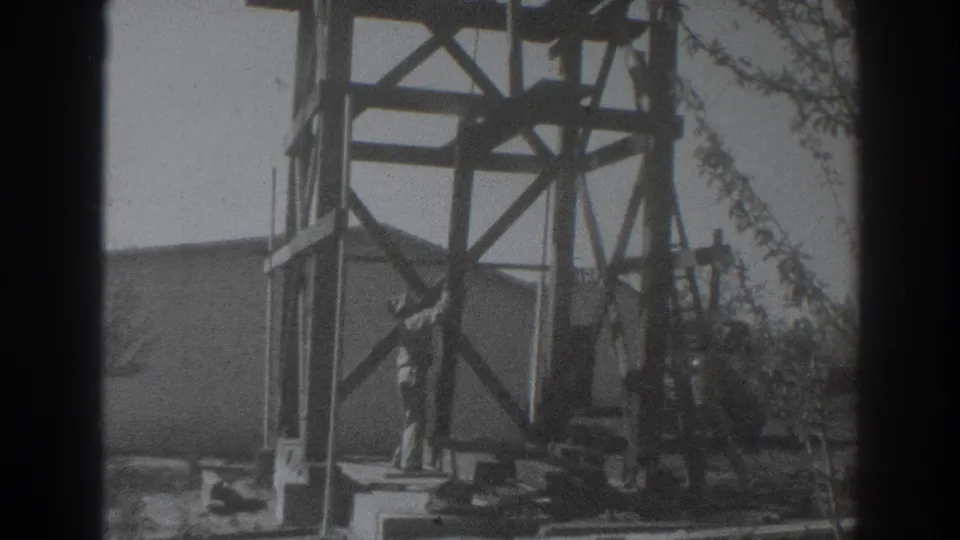 The man stands by the wooden framework in the Sacramento yard, with a board and construction materials visible around him.