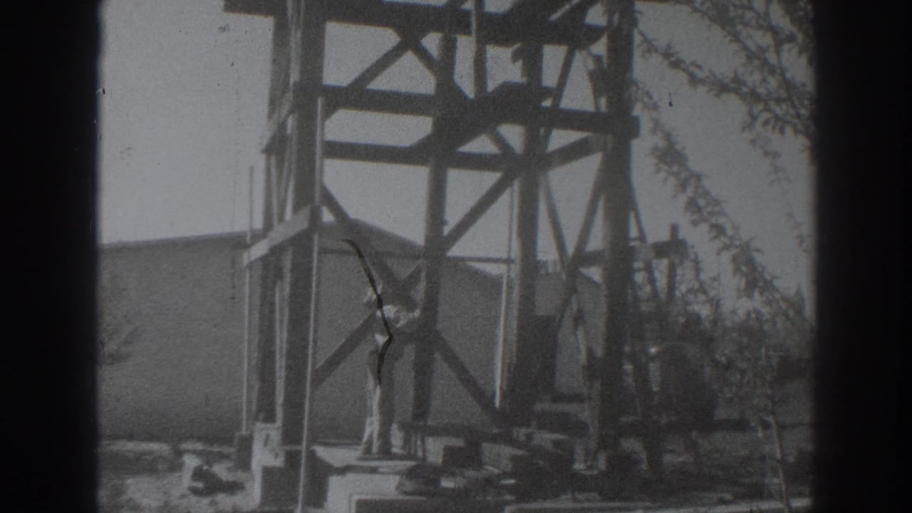 Man stands near a tall wooden construction frame with a building wall behind him.