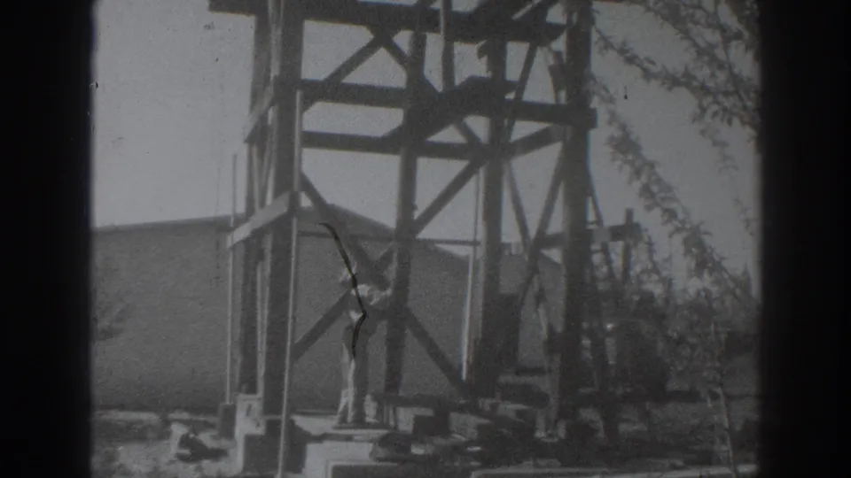 In metadata-supported 1937 Sacramento footage, a man in light work clothes stands beside a wooden frame at an outdoor site.