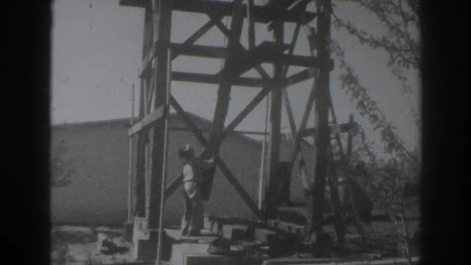 A man in light clothing raises a wooden beam on an outdoor framework in the 1937 Sacramento home-movie scene.