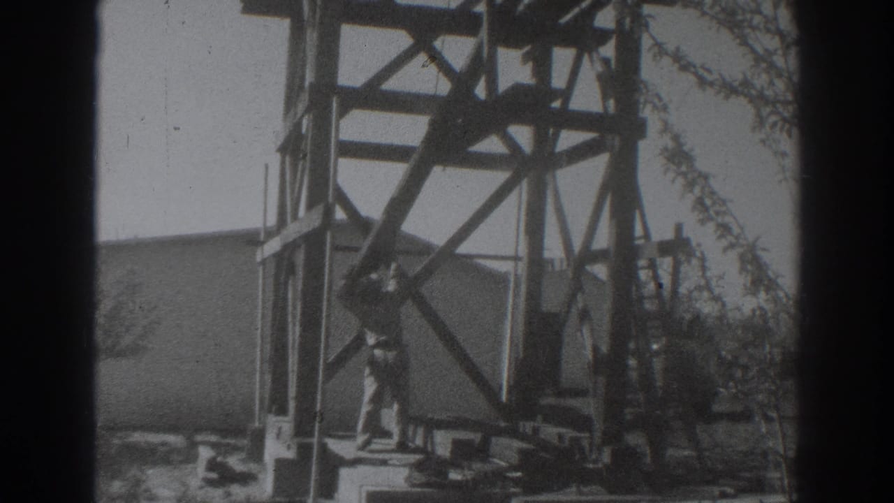Two workers stand near a wooden tower frame beside a building edge.
