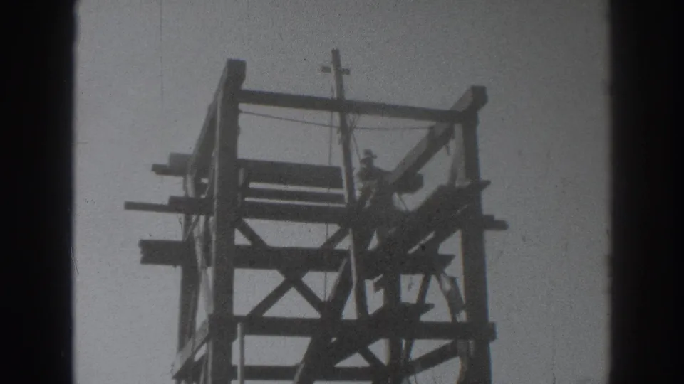 1937 Sacramento footage shows a worker elevated on a wooden framed structure with cross-bracing and upright posts.