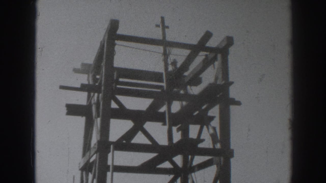 Wooden tower frame seen from below with a silhouetted worker near the top.