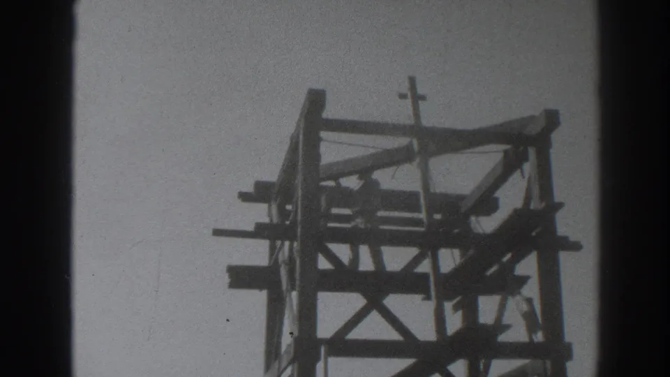 In 1937 Sacramento footage, a man appears within a wooden tower frame below a small crucifix against the sky.