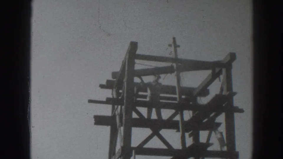 Low-angle 1937 Sacramento frame showing a man within the upper wooden structure and crucifix at the top.