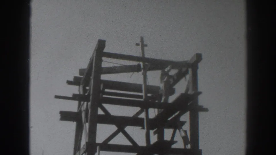 A 1937 Sacramento frame shows the worker inside the upper wooden tower, surrounded by beams with a crucifix above.