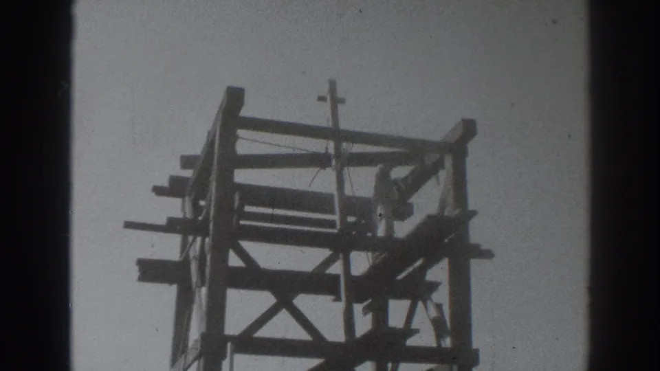 The Sacramento oil-rig frame appears in soft black-and-white 8mm, with timber beams, diagonal supports, and a small top cross element.