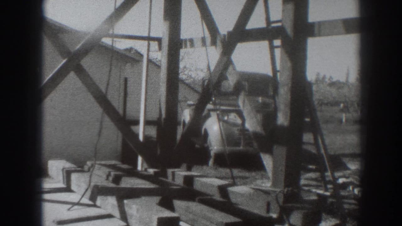 Wooden framework and work materials with a vintage car partly visible behind the structure.