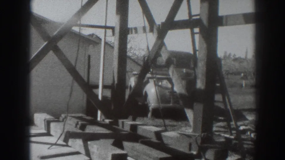 1937 Sacramento home-movie frame showing timber framing, planks, and a partially hidden vintage car in a rural work area.
