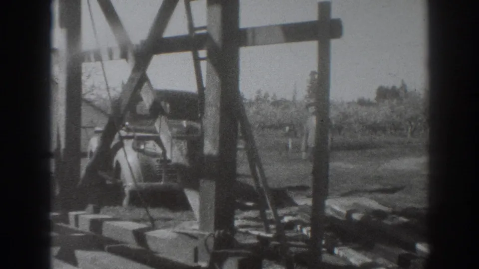 1937 Sacramento farm construction frame with an adult worker near timber framing, work materials, and orchard ground in the background.