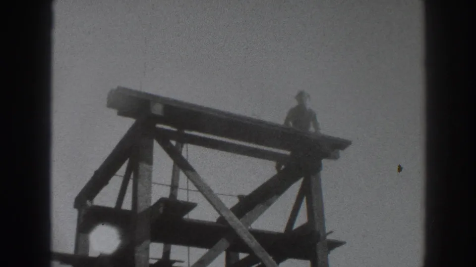 1937 Sacramento 8mm frame with a distant worker on a high timber scaffold, surrounded by beams and diagonal supports.