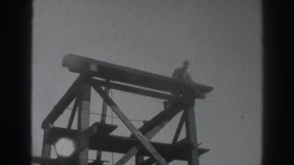 1937 Sacramento frame showing a distant worker near the right edge of an elevated wooden scaffold, with heavy bracing below.
