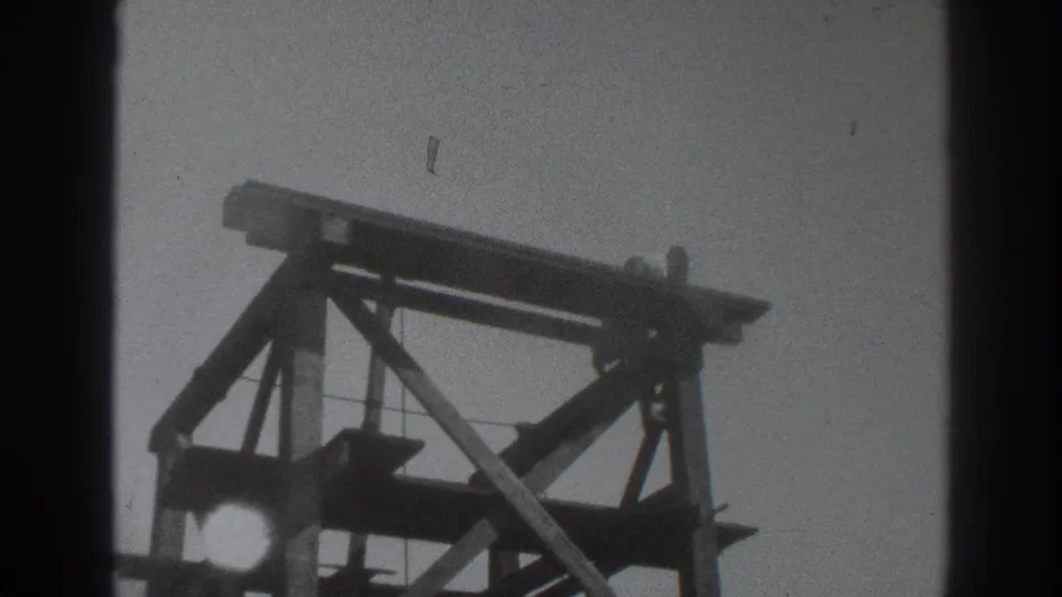 1937 Sacramento 8mm frame showing dark wooden scaffold framing against a pale sky, with no worker clearly visible in this still.