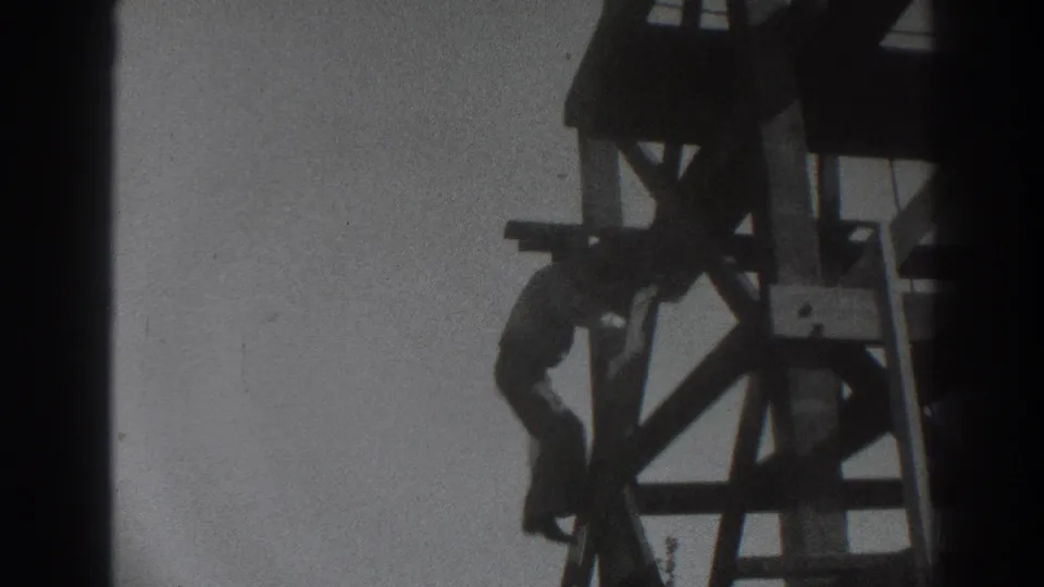1937 Sacramento 8mm frame showing a worker climbing along the side of a tall wooden scaffold structure.