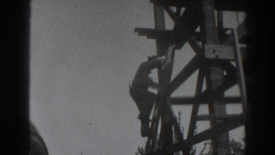 A worker climbs through wooden scaffolding in a grainy 1937 Sacramento home-movie frame, partly hidden by the structure and film edge.