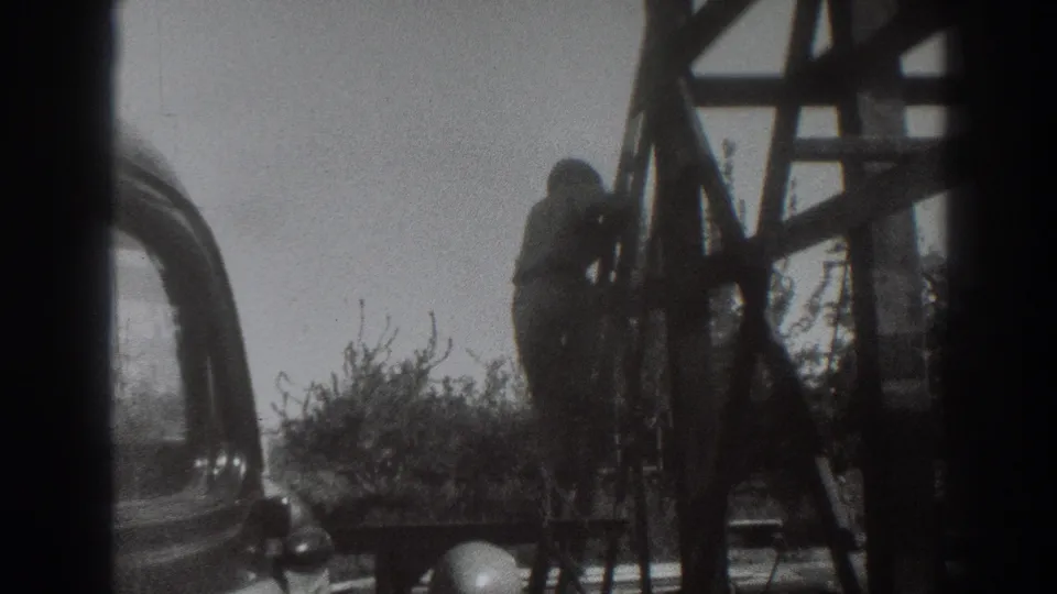 The man is seen higher on the wooden structure, with part of an old automobile and brush visible in Sacramento, 1937 metadata.