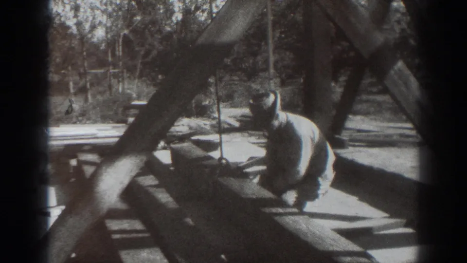 In 1937 Sacramento home-movie footage, a man kneels by heavy timber beams on an outdoor wooden structure.