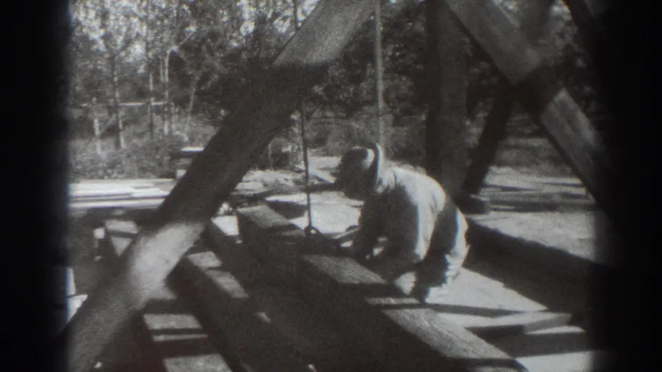 A man in work clothes kneels on or beside a timber framework in archival 1937 Sacramento footage.