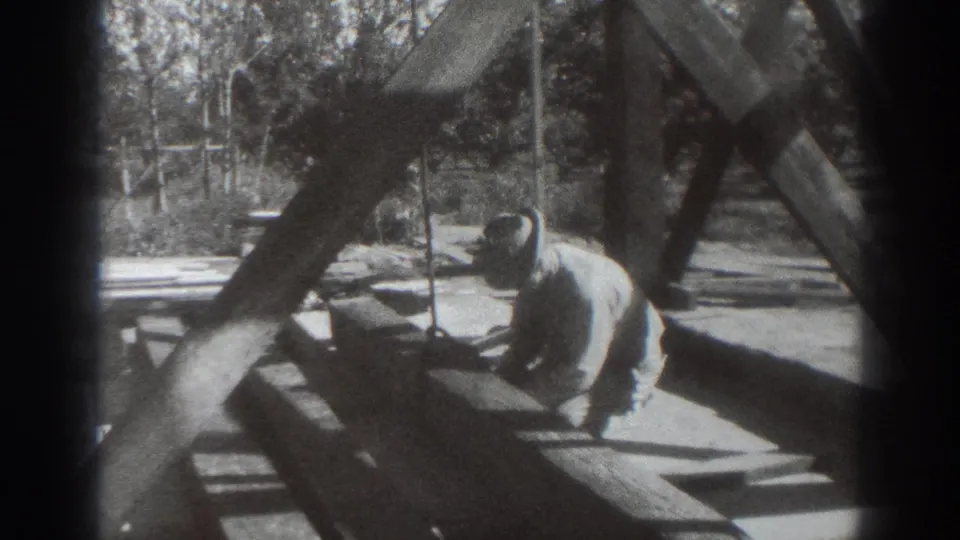 The man appears to glance toward the camera while kneeling beside a rustic wooden structure in Sacramento.