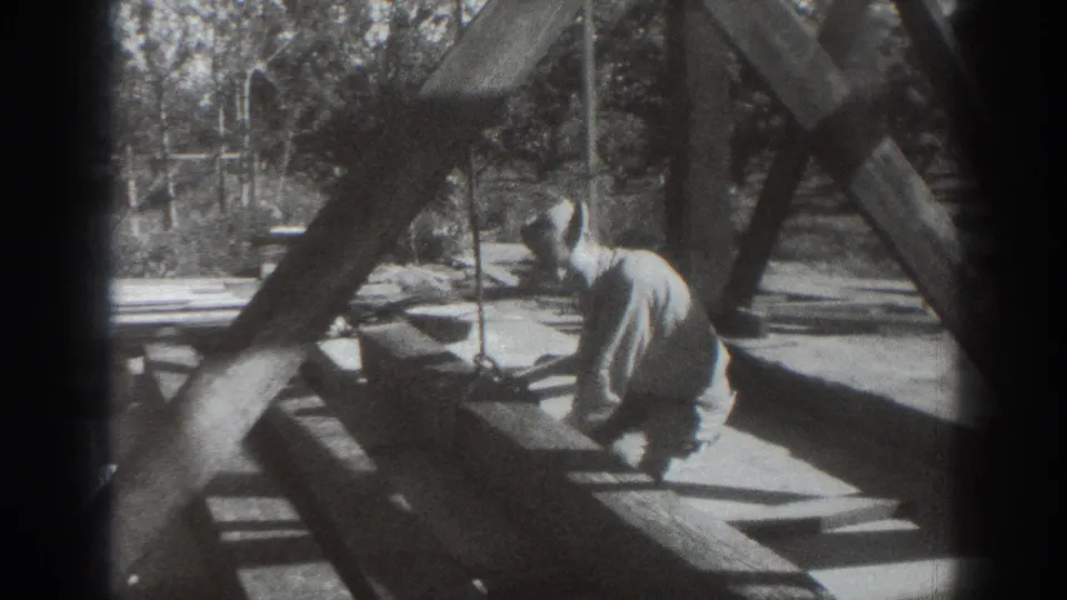 The worker kneels under angled wooden supports, with rope visible beside the beam structure in the Sacramento 1937 clip.