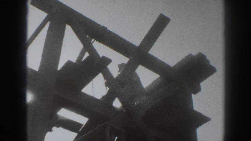 The 1937 Sacramento footage shows the worker moving along the frame, his body partly hidden by timber members.