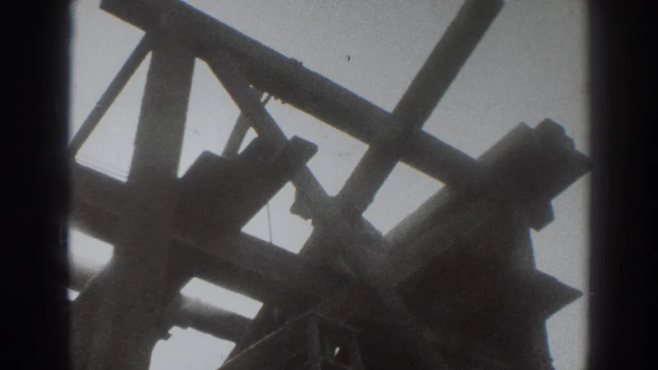Low-angle 8mm frame of a Sacramento construction worker among timber supports, backlit by the sky.