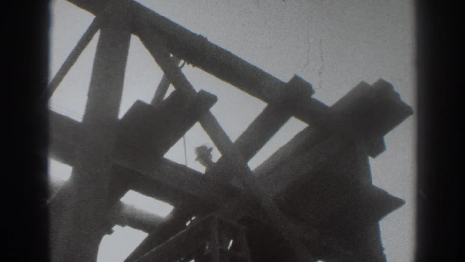 Sacramento 1937 home-movie frame showing a worker moving within a dark wooden construction frame against the sky.