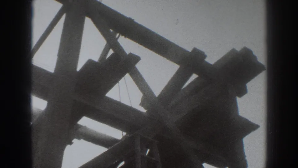 1937 Sacramento 8mm frame showing a low-angle view of heavy wooden beams, diagonal braces, and hanging lines against an overcast sky.