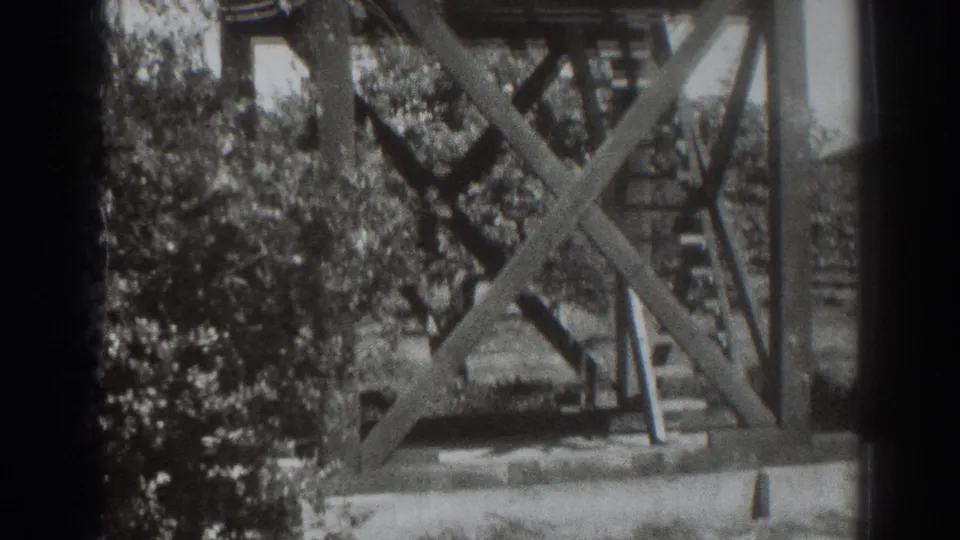 Wider 1937 Sacramento frame showing a wooden braced structure on a raised base, with trees and a ladder-like element nearby.